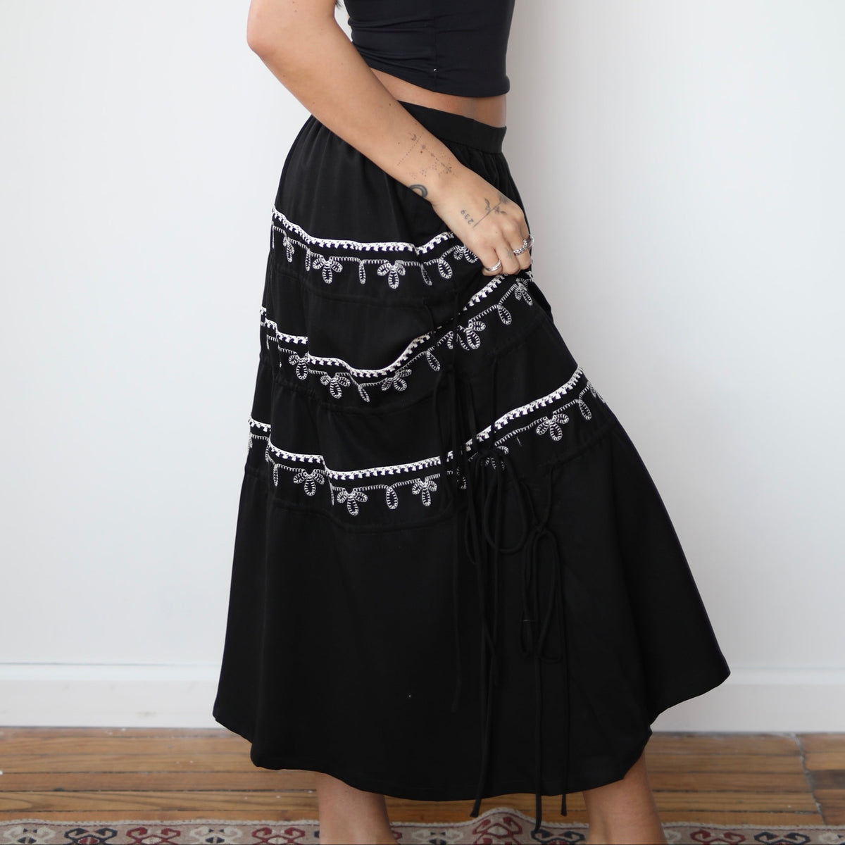 Woman wearing a black outfit with white embroidery and a white hat against a white background