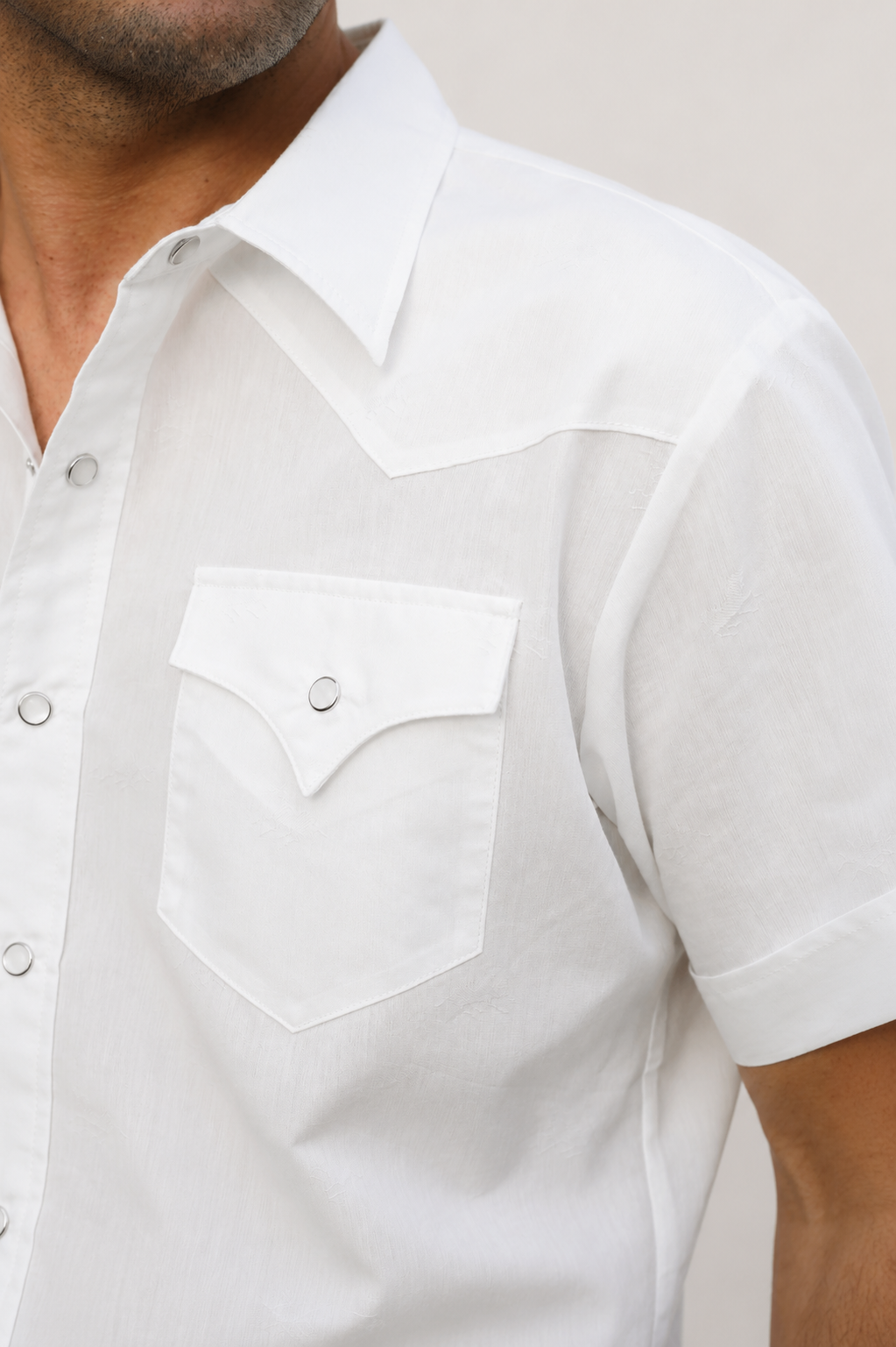 Close-up of a man wearing a white short-sleeve western-style button-up shirt with a pointed collar, chest pocket, and snap-button flap.