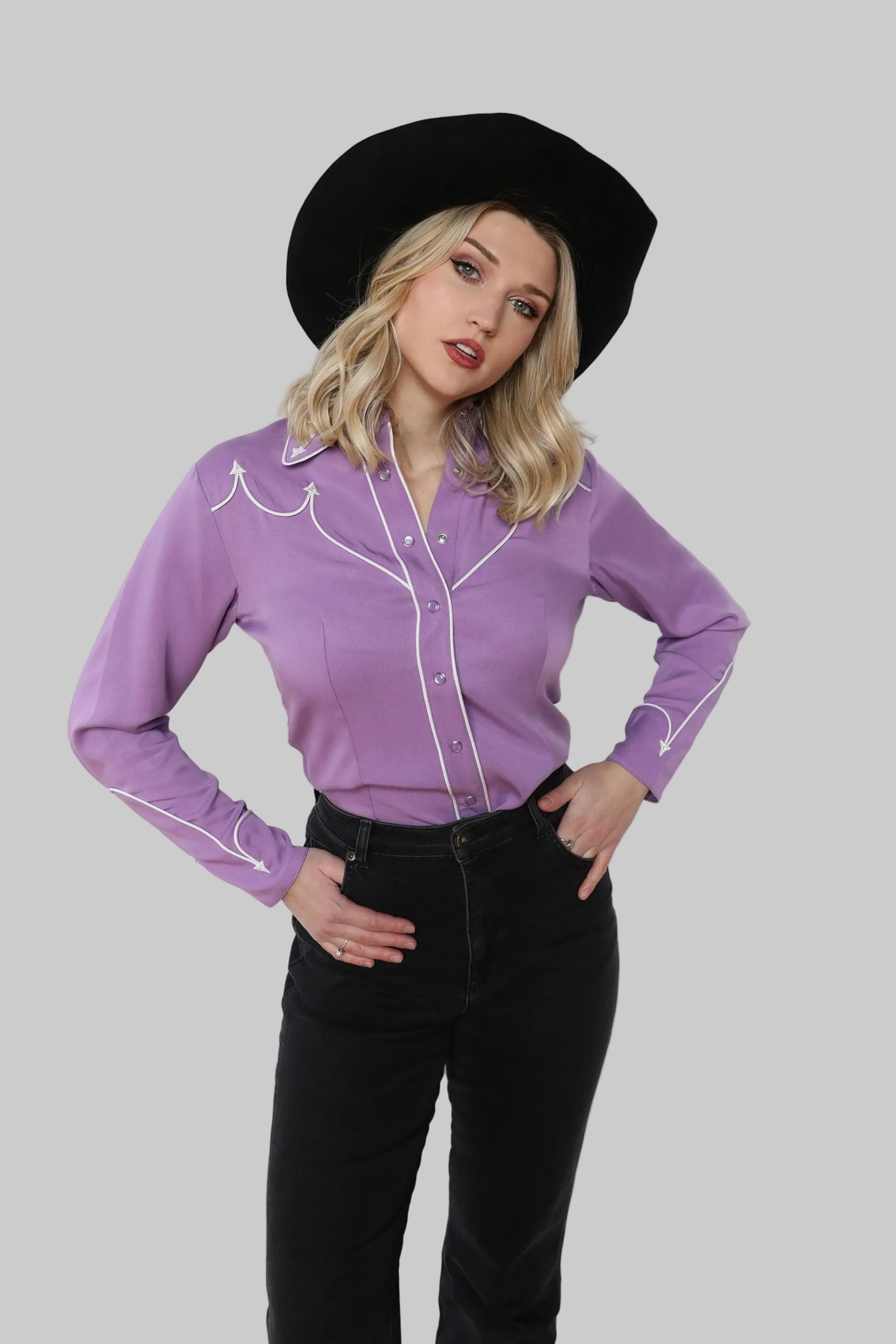 Woman wearing a purple western shirt with white trim and black pants against a white background