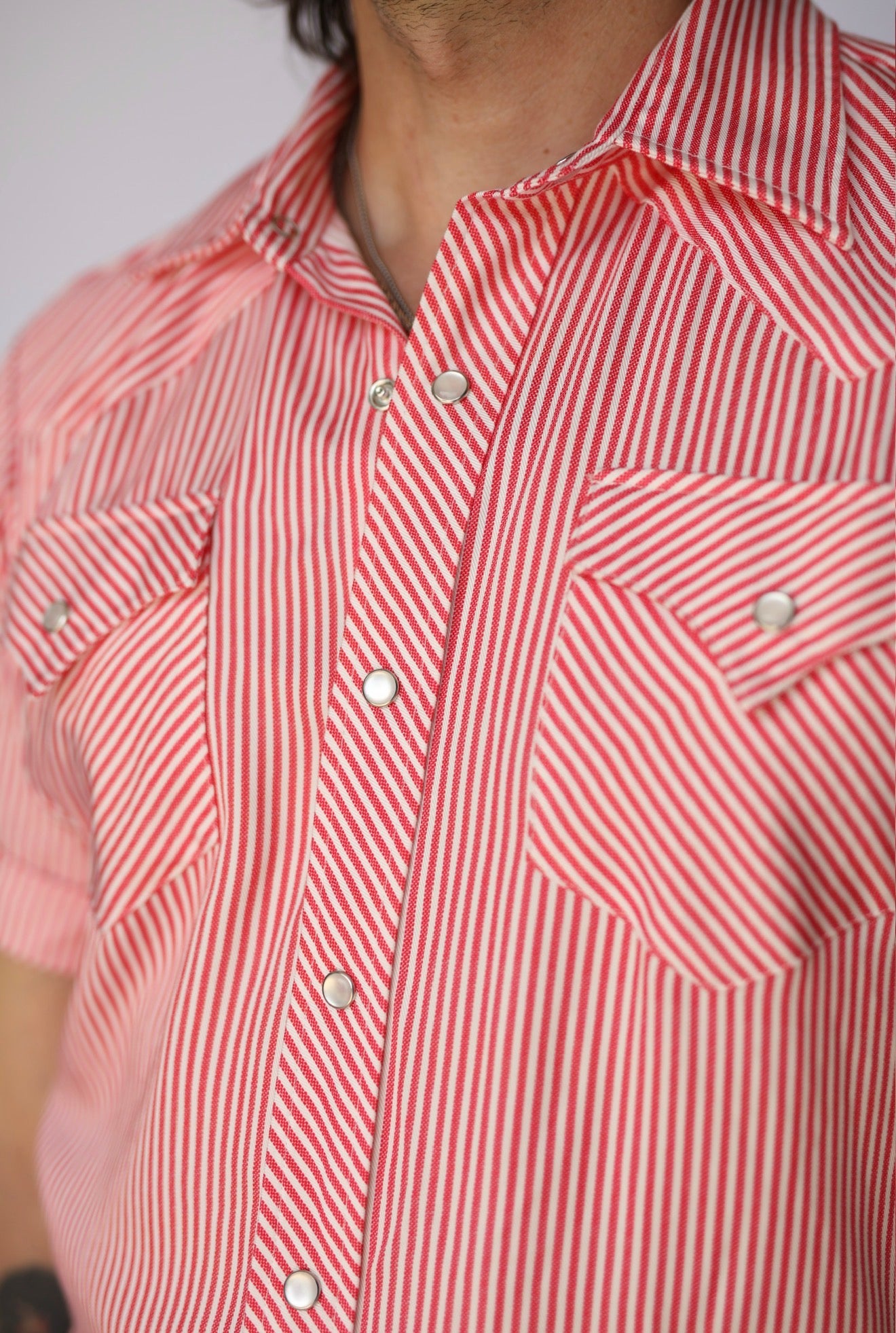 A close-up of a man wearing a short-sleeve button-up shirt with diagonal red and white stripes, featuring two chest pockets with silver snap buttons.