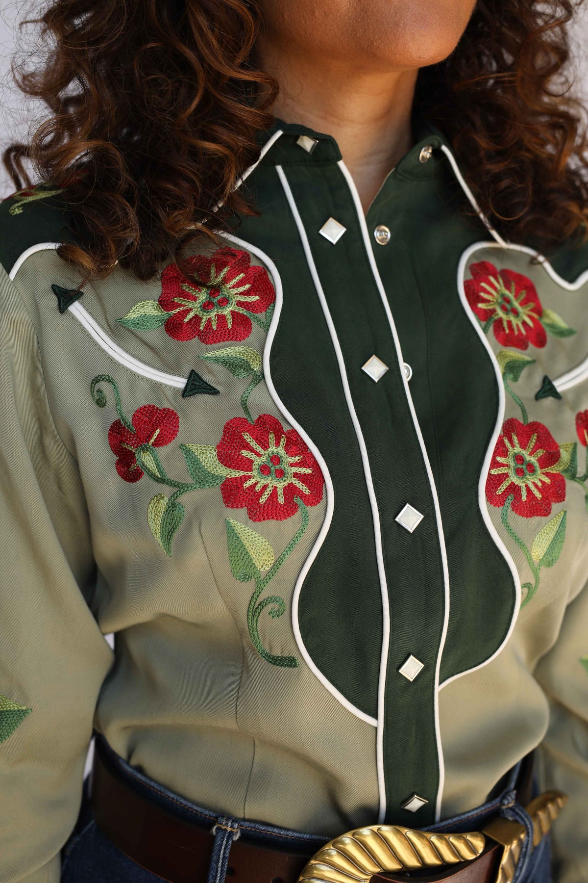 Close-up of the H Bar C Santa Ana green shirt front showing red floral embroidery, white piped smile yoke, and diamond pearl snaps, vintage inspired western wear.