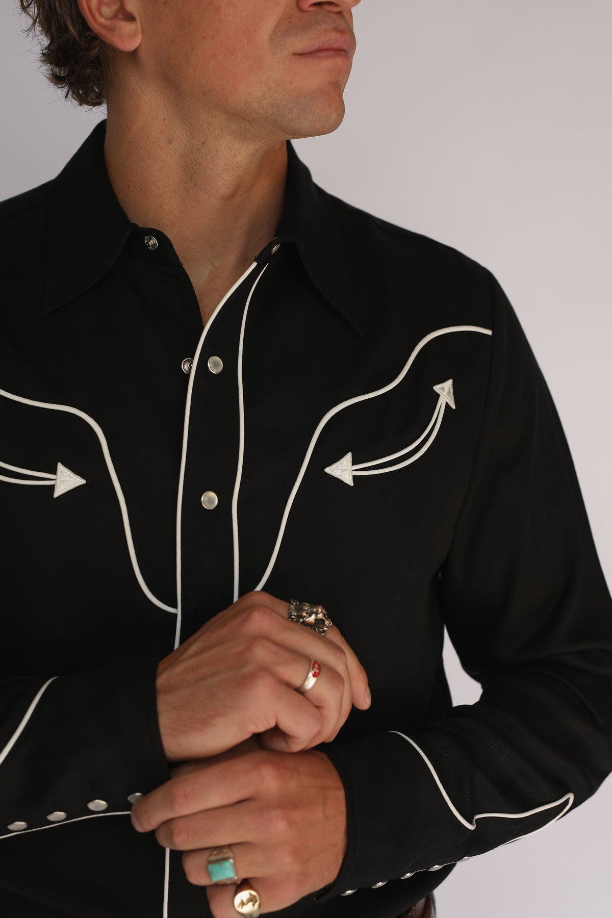 Model adjusting the collar of the H Bar C San Fernando black shirt, vintage western wear with white piped yoke and pearl snap placket.