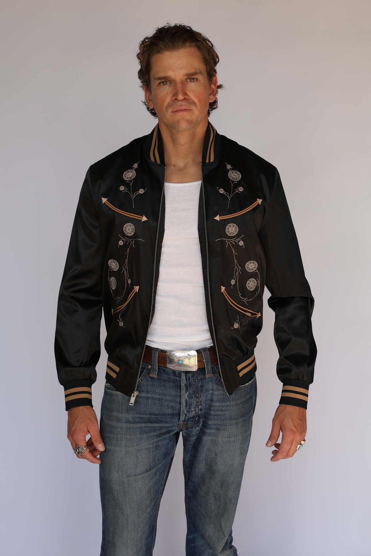 Front view of the H Bar C x Gibson J-200 Odessa jacket open over a white tank, vintage western wear with tan floral embroidery, arrow pockets, and striped trim.