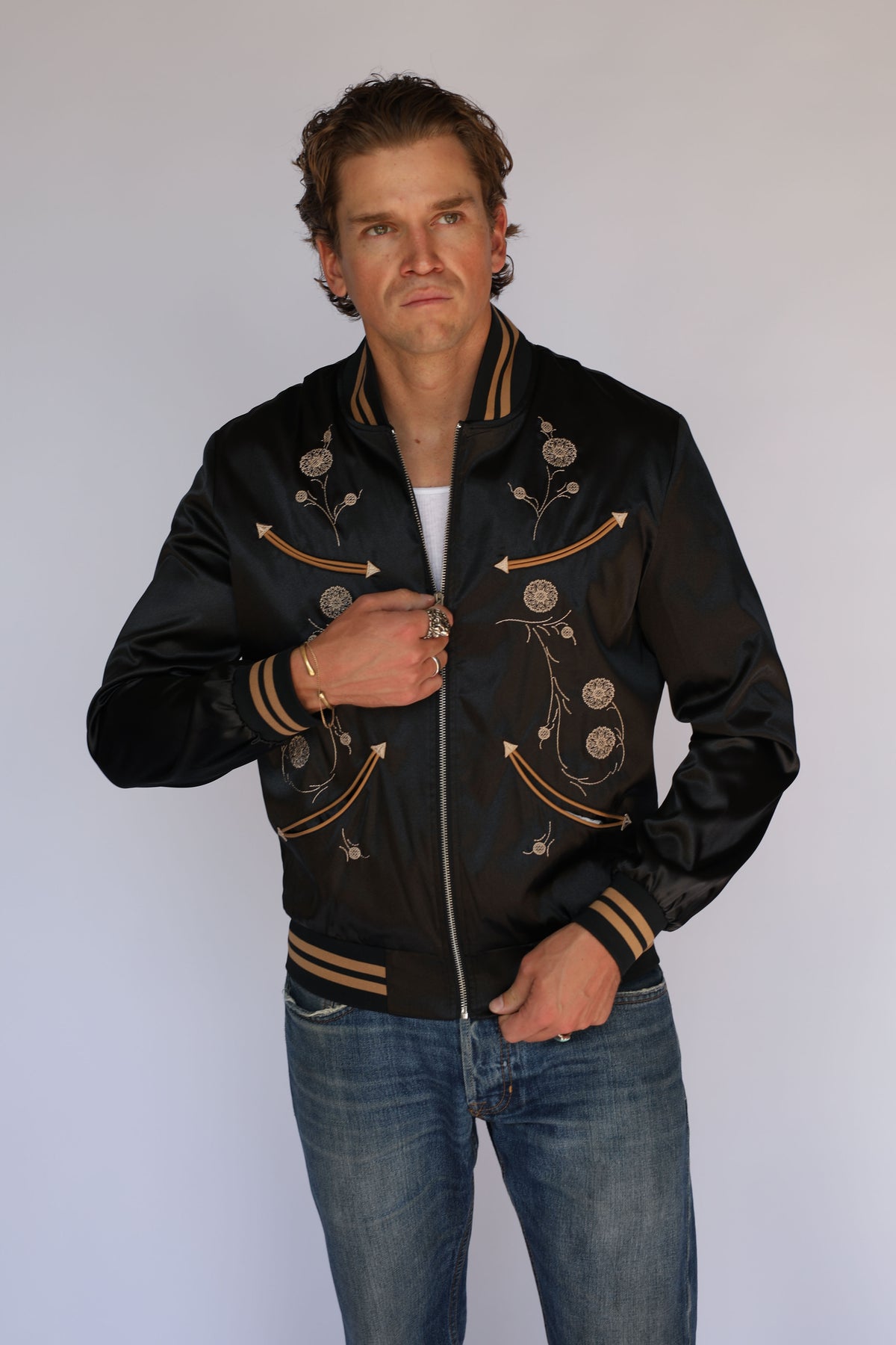 Man wearing the H Bar C x Gibson J-200 Odessa jacket in black satin, vintage inspired western wear with Gibson J-200 floral embroidery and tan arrow pockets.