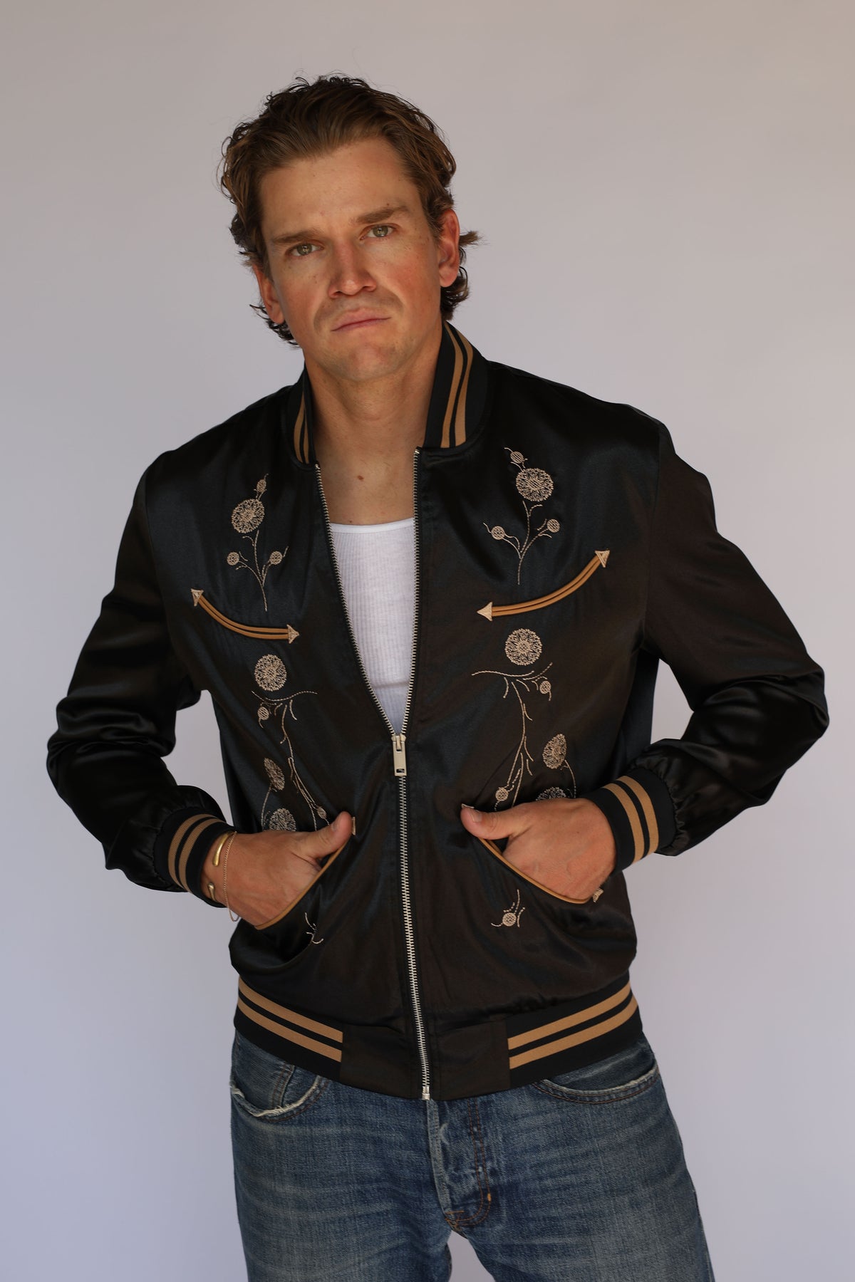 Man wearing the H Bar C x Gibson Odessa black jacket with hands at the zipper, vintage western wear with tan floral embroidery.