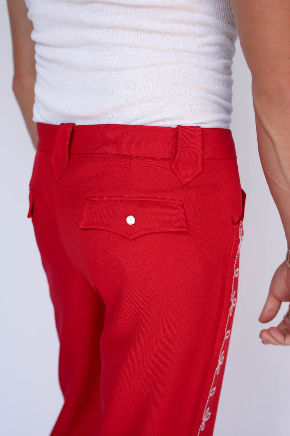 A person modeling bright red straight-leg western pants with a white flower embroidery down the leg.