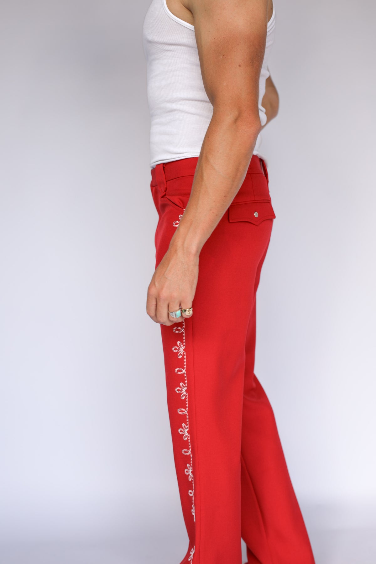A person modeling bright red straight-leg western pants with a white flower embroidery down the leg.