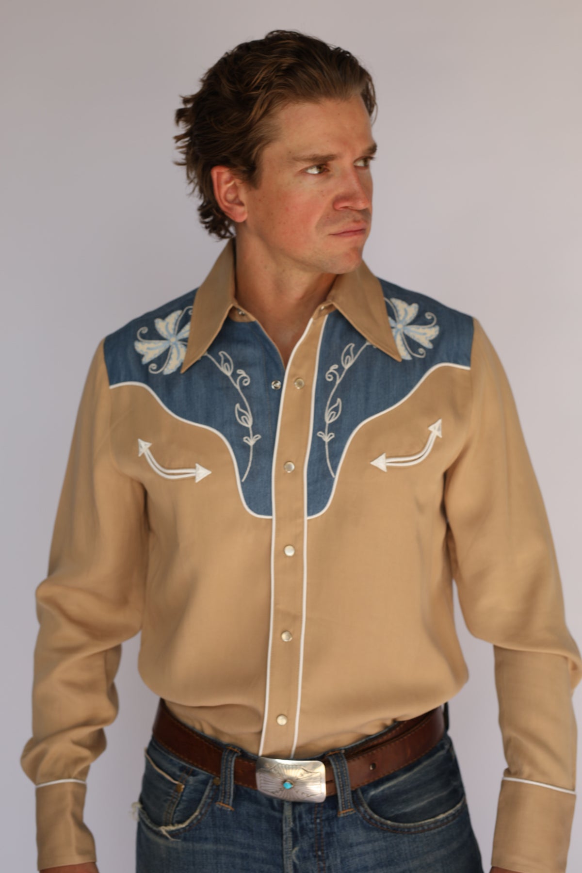 Man wearing the H Bar C Telluride tan western shirt, vintage inspired western wear with a denim yoke, white floral embroidery, and pearl snaps.