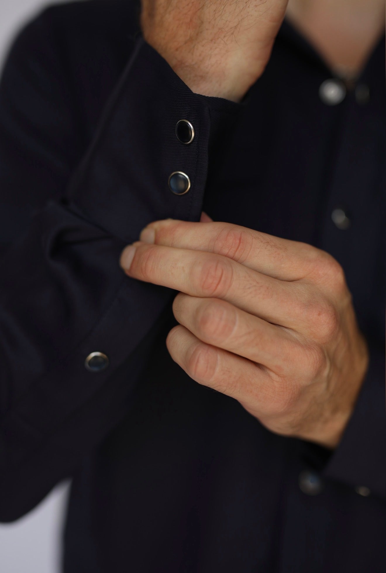 Close-up of a person's hands adjusting the cuff of a dark navy blue button-down shirt, showing silver snap buttons.