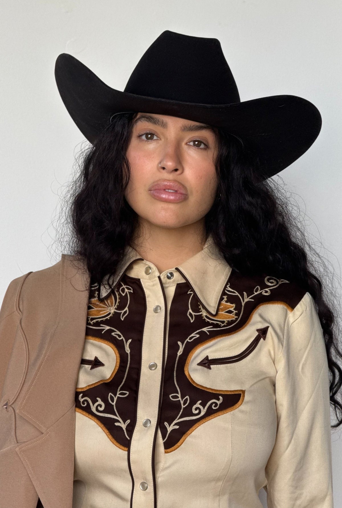 Person wearing a black cowboy hat and a beige H Bar C shirt with intricate chain stitch designs against a white background