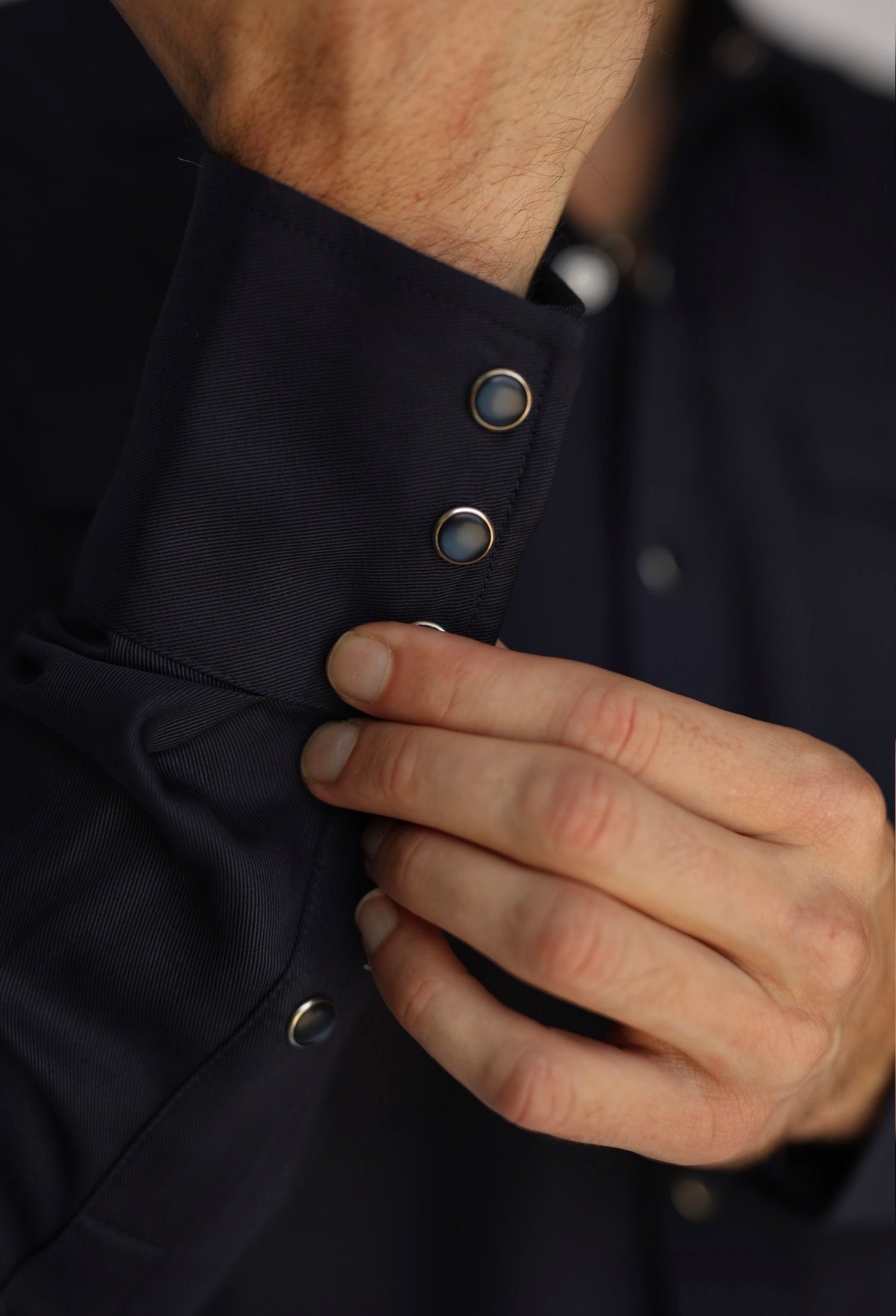 Close-up of a person's hand adjusting the buttoned cuff of a dark navy long-sleeve shirt.