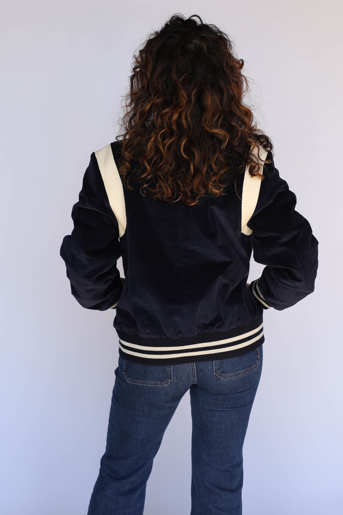 Back view of the H Bar C Silver Lake navy corduroy jacket on a woman, showing cream shoulder panels and striped ribbed waistband.