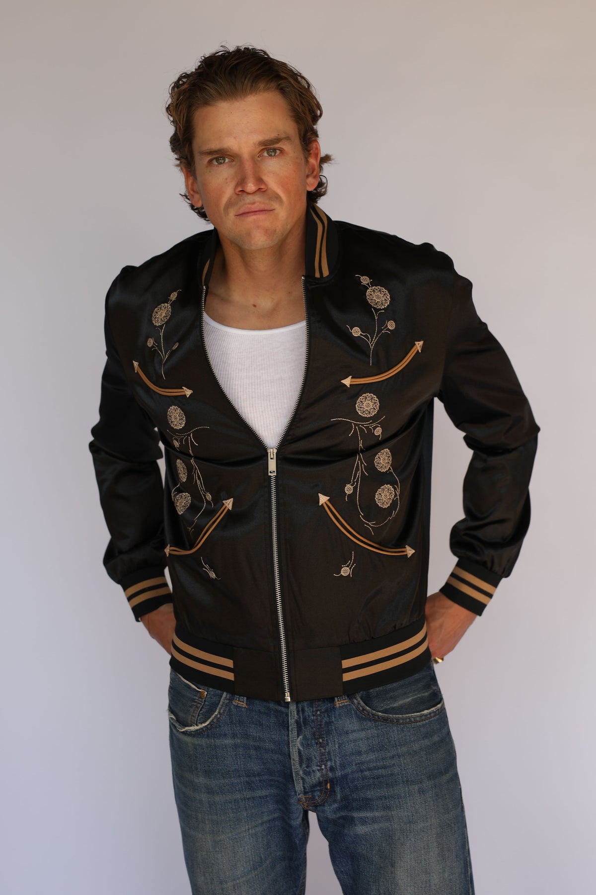 Model holding the front of the H Bar C x Gibson J-200 Odessa black jacket, vintage western wear with tan piped arrow pockets.