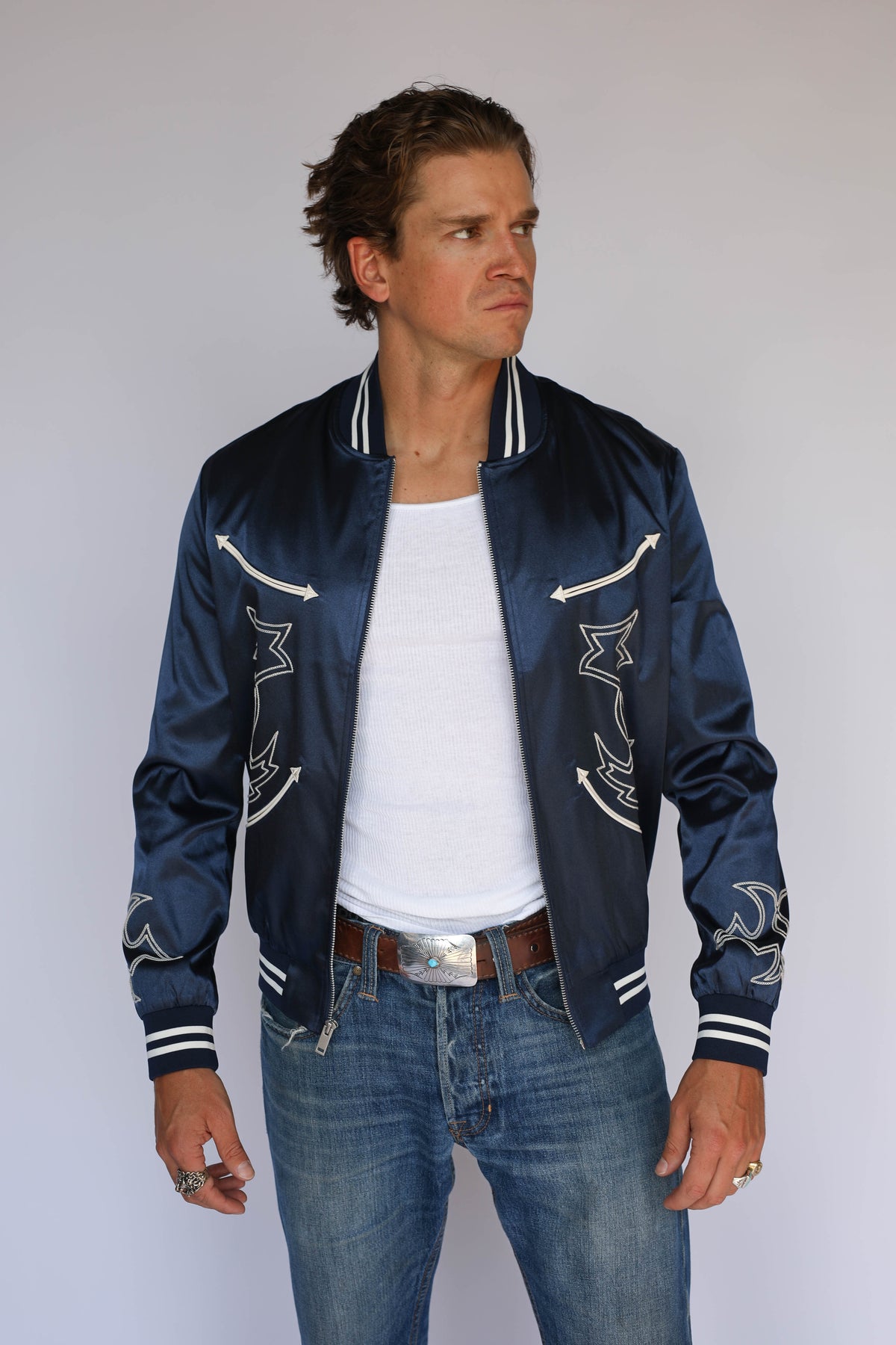 Man wearing the H Bar C Odessa Tour Jacket in navy satin, vintage inspired western wear with cream arrow appliqués and boot stitch embroidery.
