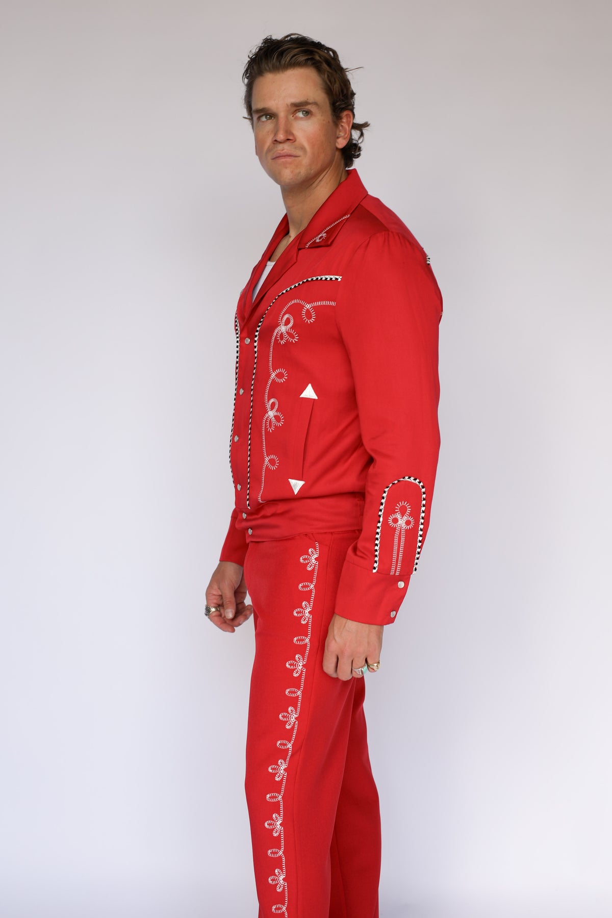A person modeling bright red straight-leg pants with a white flower embroidery down the leg. 