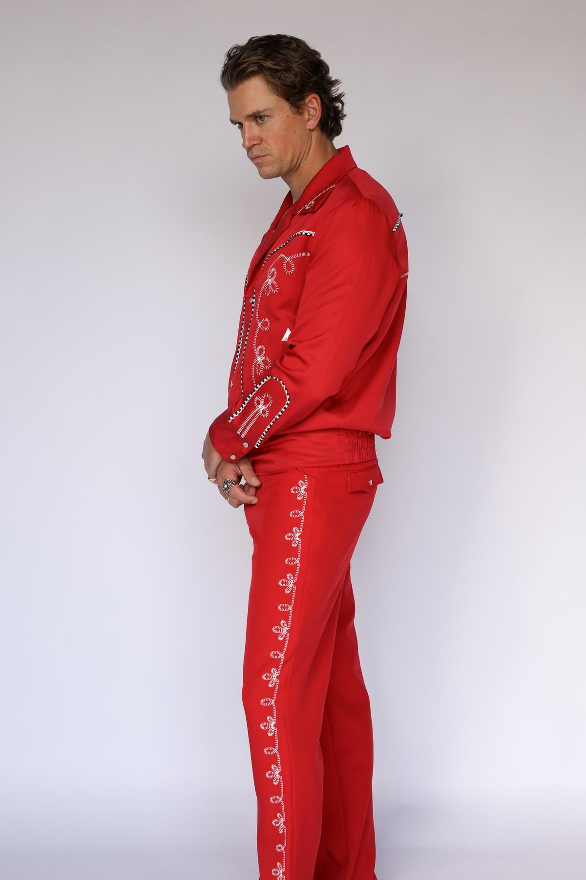 A person modeling bright red straight-leg western pants with a white flower embroidery down the leg. 