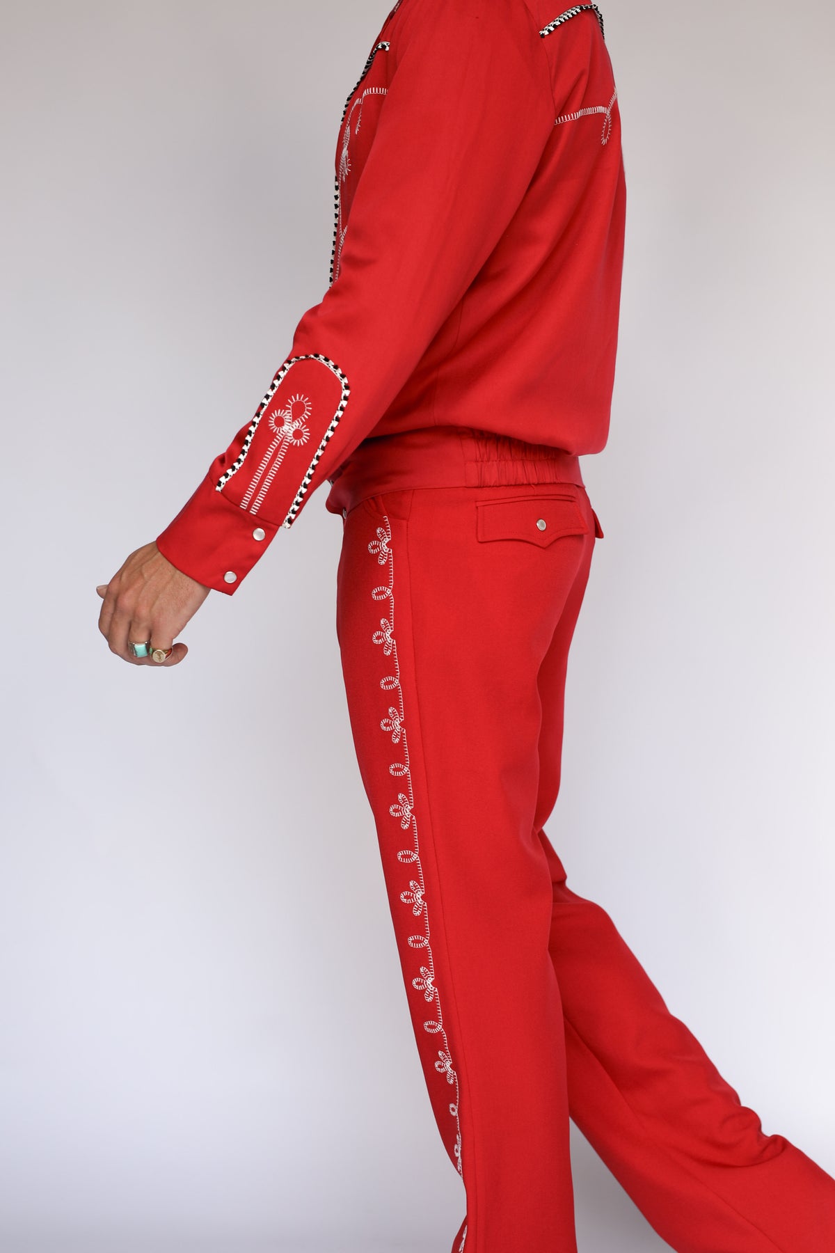 A person modeling bright red straight-leg western pants with a white flower embroidery down the leg. 