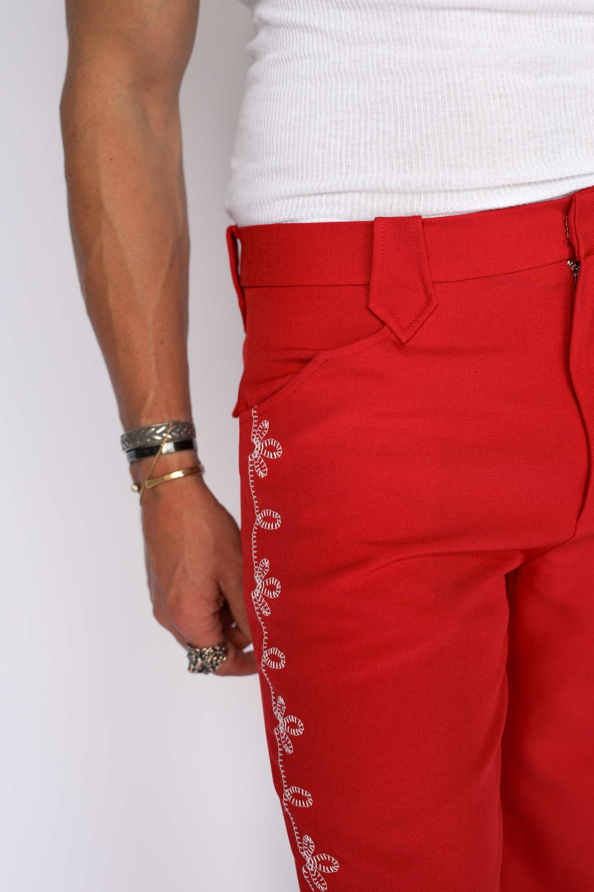 A person modeling bright red straight-leg western pants with a white flower embroidery down the leg. 