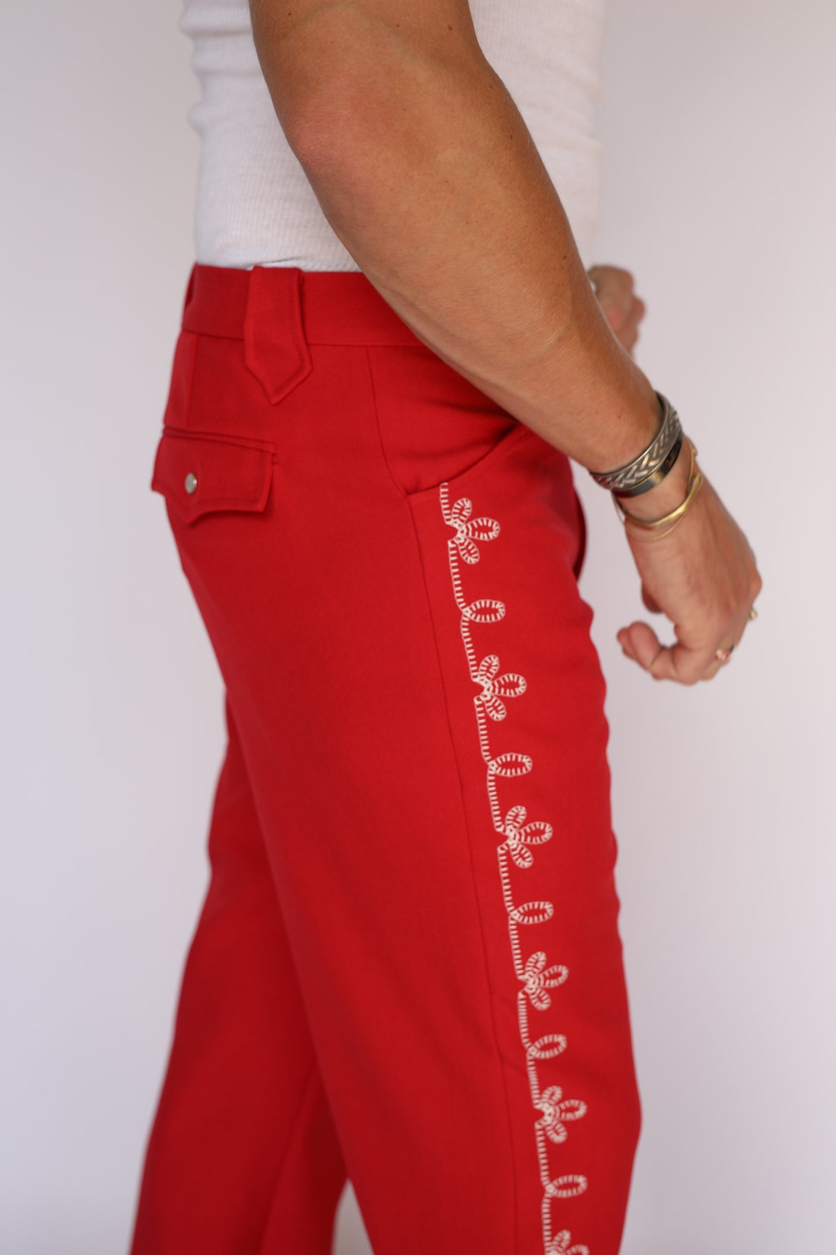 A person modeling bright red straight-leg western pants with a white flower embroidery down the leg. 