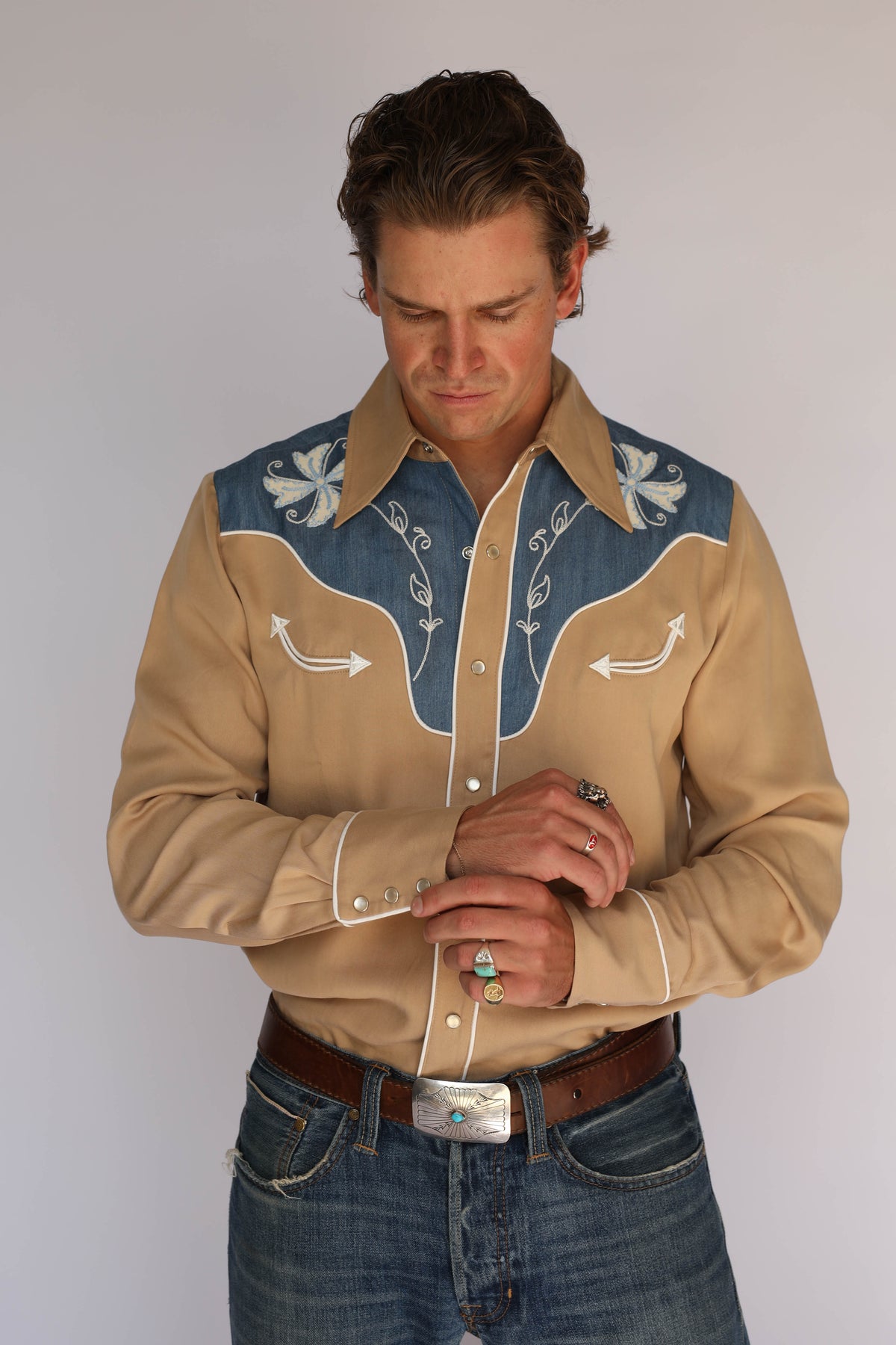 Man in the H Bar C Telluride western shirt with hand at his belt, showing the denim yoke and white floral embroidery, vintage western wear.