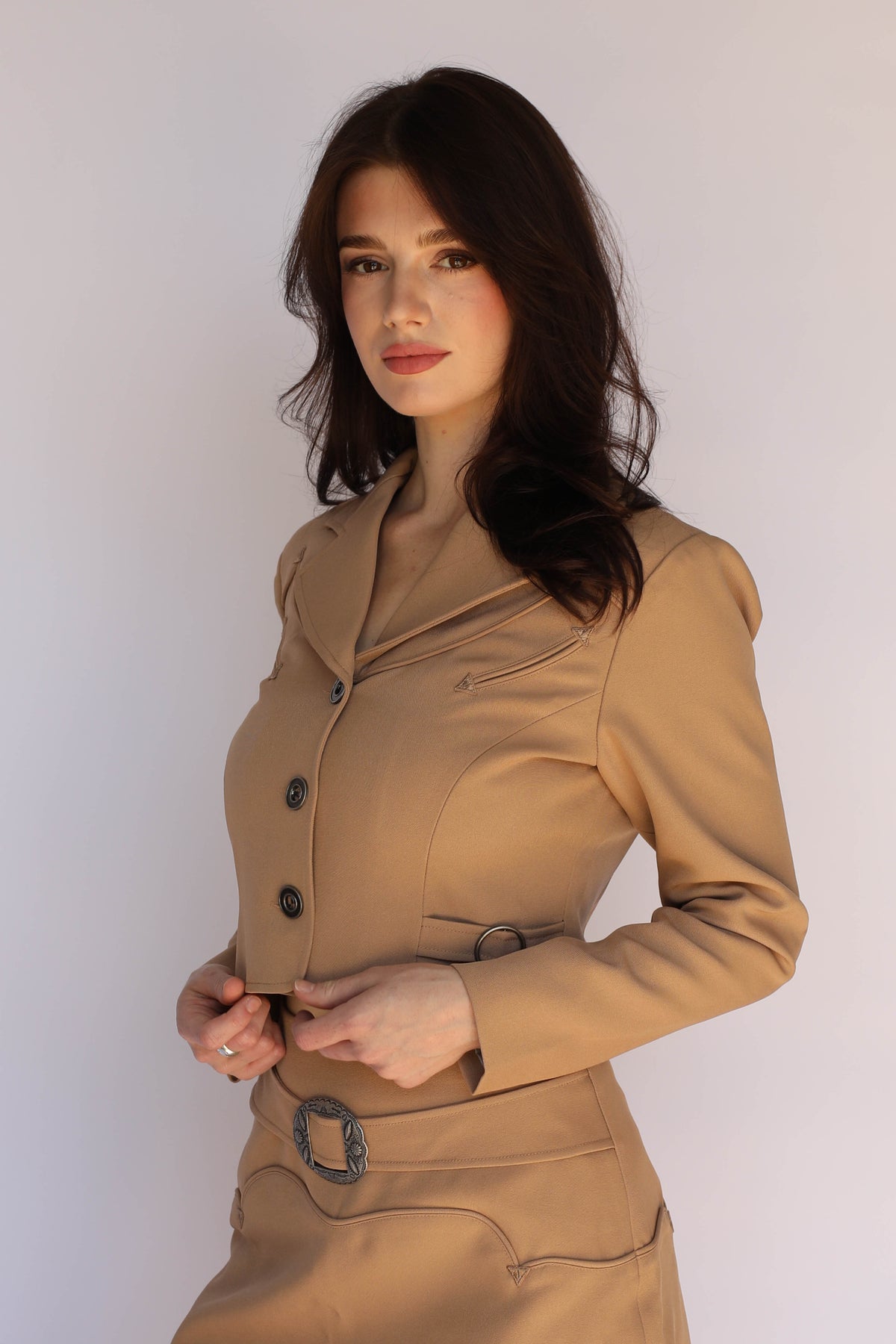 Woman wearing the H Bar C Raleigh tan cropped western jacket with arrow pocket details and matching belted skirt with concho buckle, vintage inspired western wear.