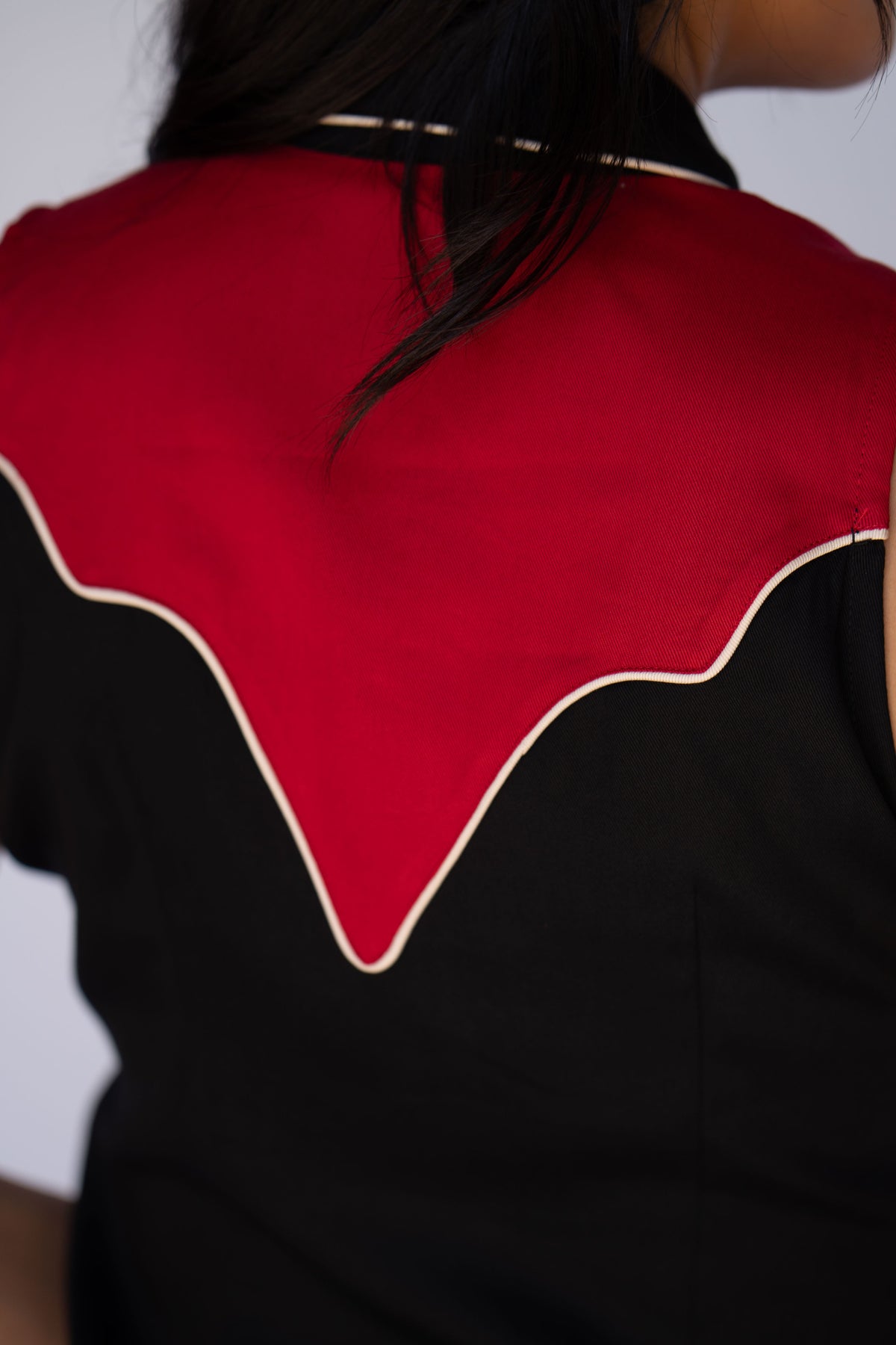 Close-up back view of a person wearing a black and red garment with a bold red yoke outlined in cream piping.
